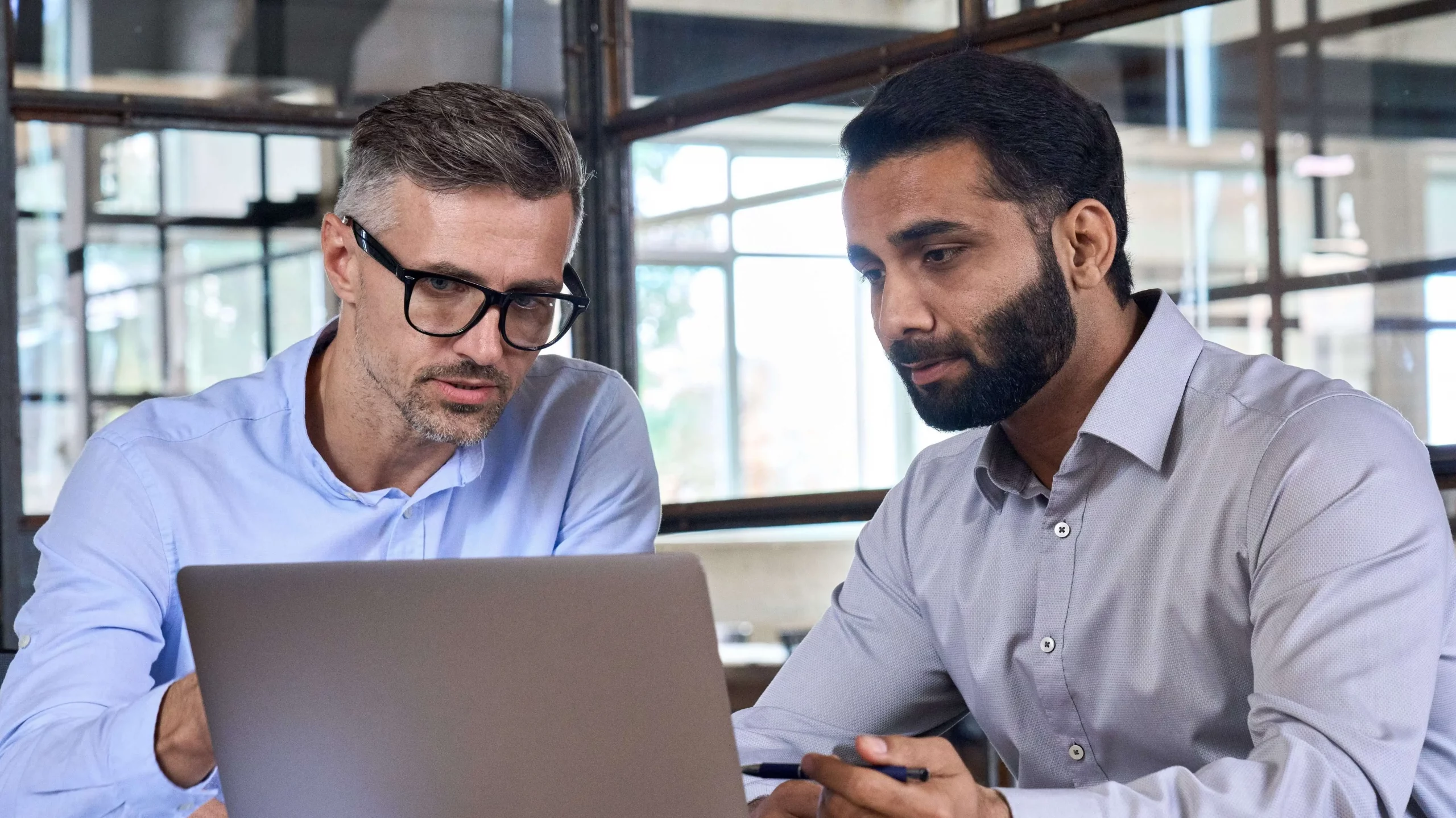 Two men sit in front of a grey laptop computer.