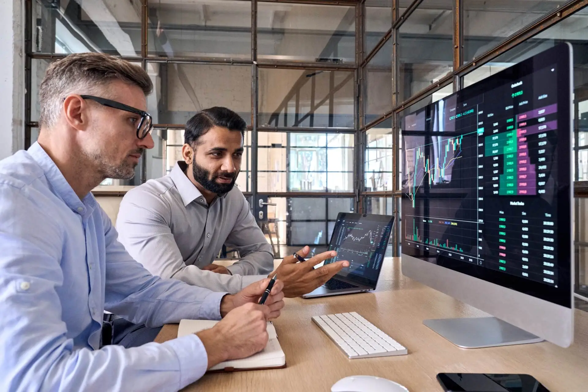 Two businessmen are looking at a computer screen. On the computer screen is a graph of their businesses profitability over the last few quarters. They are considering how to invest business profits to avoid taxes.